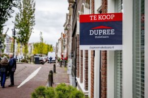 Een koopwoning met een verkoopbord van een makelaar.
